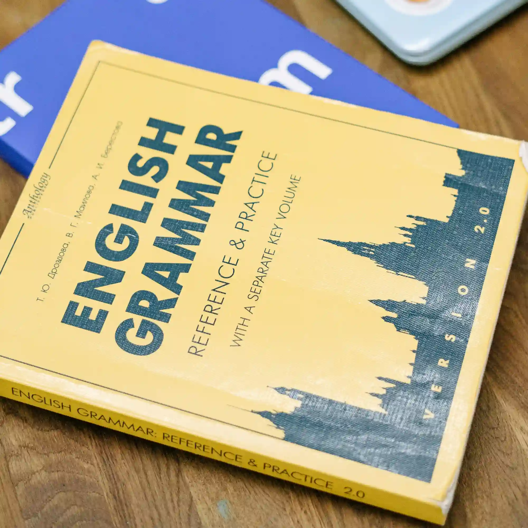 Primo piano di un libro di testo giallo intitolato 'English Grammar: Reference & Practice' appoggiato su un tavolo di legno, utilizzato come supporto fondamentale per l'apprendimento nei corsi di lingua.
