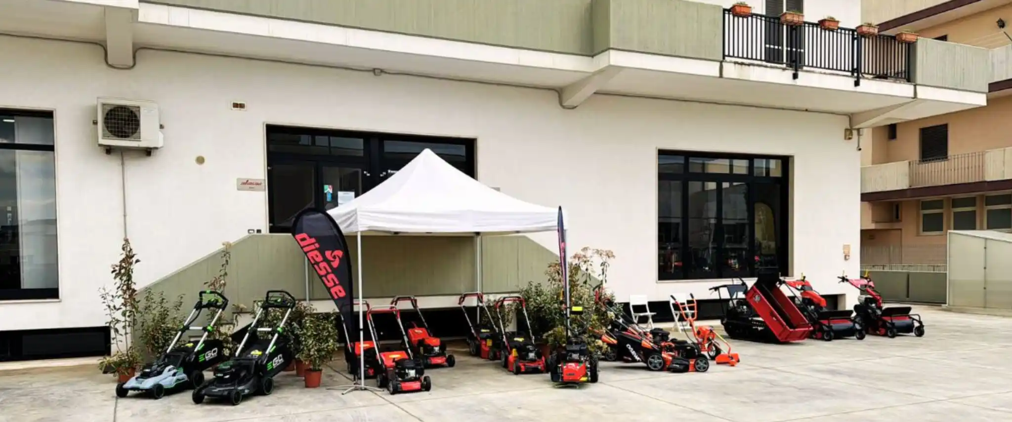 Piazzale esterno del punto vendita Diesse Agri allestito con un gazebo bianco e una vasta gamma di macchinari in esposizione, tra cui tosaerba, decespugliatori e motocarriole cingolate allineati ordinatamente.