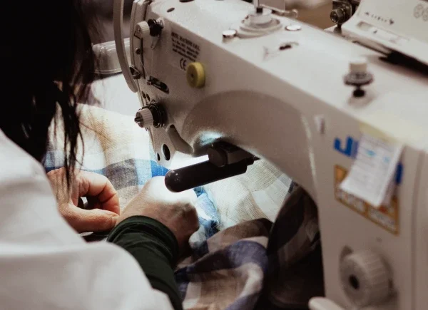 Primo piano di sarta al lavoro con macchina da cucire in laboratorio artigianale